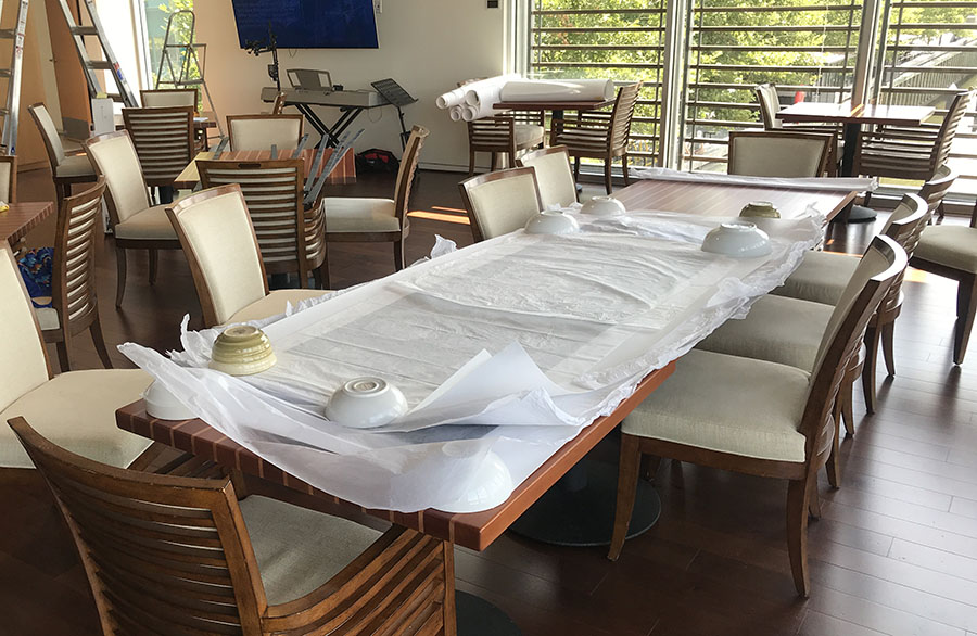 Large Photo Prints Unrolled from Storage and Flattening on Tables Under Bowls and Tissue Paper.